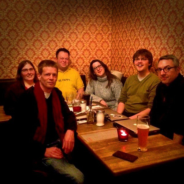 sechs Personen sitzen in einem Café um einen Tisch und lächeln in die Kamera